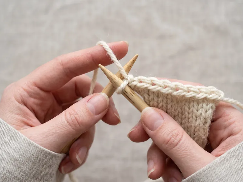 Close-up macro of binding off: lifting the back stitch up and over the front stitch on the knitting needle